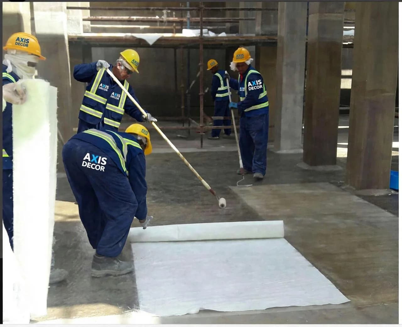 Crew applying GRP waterproofing membrane on a concrete floor